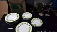 Several stacks of plates with green foliage and tiger decoration on rim, arranged on dark surface