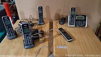 Five Panasonic phone handsets shown with cords and a base unit on a wooden table, accompanied by phone chargers and a wired headset.
