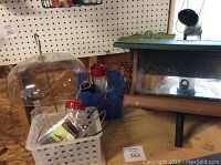 Photo shows three bird feeders and a blue container with parts, situated on a cardboard surface with pegboard background.