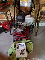 Front view of red and black Generac unit with owner’s manual in green bag at base