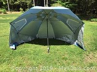 Gray beach tent setup outdoors on grass, showing side windows and a central pole.