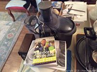 Black Breville juicer on table with juice diet book on top.