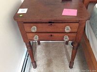 Front view of antique wooden end table with two drawers and glass knobs, showing wear and leg details.