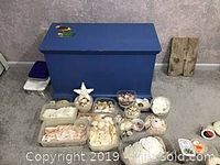 Containers with assorted seashells and starfish displayed outside the opened chest on carpet, showing the variety and quantity of shells.