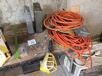 Photo showing multiple orange power cords coiled on wooden table alongside metal first aid kit and another container.