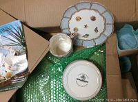 Box with Seashell Isle dinnerware pieces including a plate, mug, and brochure