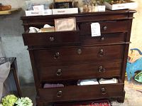 Front view of wooden dresser showing two smaller top drawers and three larger bottom drawers with metal ring handles. Some drawers are partially open revealing contents that are not included.