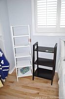 Photo showing both ladder shelves side by side on wooden floor near window and bed.