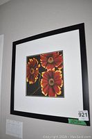 Square floral print of three reddish-orange flowers with yellow tips in a black frame with white matting