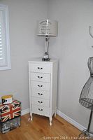 Full view of white lingerie chest with six drawers topped by Paris Metro lamp
