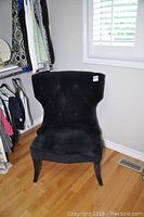 Front angled view of the black velvet accent chair showing tufted backrest and wooden legs.