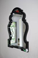 Front view of unique wood framed decorative mirror showing ornate curved black frame and clear mirror reflecting front door with stained glass.
