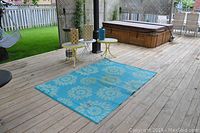 Outdoor deck setting with blue floral rug, round yellow metal tables, plant stand, and decorative accent items.