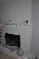 Wide view of mantel and hearth with various glassware and ceramics displayed including goblets, bowls, plates, and cake stand.