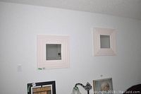 Two 24x24 square mirrors with stepped cream colored wood frames hanging on a white wall.