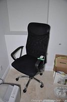 Front view of black padded seat and mesh backrest office chair with armrest and chrome base on casters.