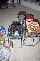 Three black metal plant stands viewed on tile floor with other household items nearby, showing lattice tops and leaf side accents.