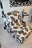 View of accent chair from a side angle showing the leaf patterned fabric and attached back cushion