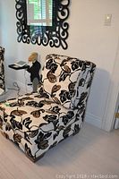 Accent chair in brown, black, ivory leaf pattern upholstery shown near a decorative mirror and side table.