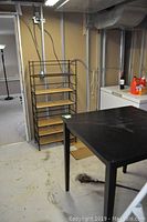 Overall view of the metal rack shelving unit and black pub height table in a basement setting.