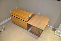 Wooden chest with rounded top and wooden side table placed on carpeted floor near wall.