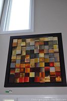 Front view of the large 40x40 square abstract art piece showing the grid of colorful square blocks in a black frame, mounted on a wall beneath a window.
