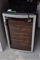 Front view of the stainless steel bar fridge with glass door and visible internal wire racks.