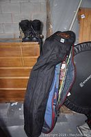 Two black protective snowboard cases leaning against a wall with a pair of black snowboard boots on a wooden surface nearby