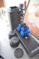 Photo of aerobic step platform, stack of risers, black weight plates, and rack of blue dumbbells.