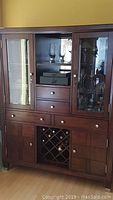 Front view of the solid wood dining cabinet showing glass doors with adjustable shelves inside, drawers, cupboards, and wine rack at the bottom.