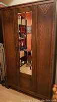 Front view of antique wooden armoire with beveled mirror door and carved wood designs on both side doors.
