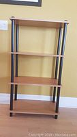 Front view of wooden shelving unit showing four shelves and black metal supports against a beige wall.