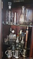 Overall view of glass decanters, pitcher, pewter beer steins, copper martini shaker, metal bar tool set with swizzle sticks