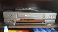 RCA VCR player with remote on top, showing front panel with controls and VHS slot