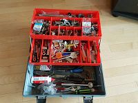 Metal gray Mastercraft tool chest opened showing red plastic organizer tray filled with nuts, bolts, and small hardware components. Bottom tray contains hand tools such as pliers and wrenches.
