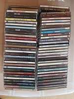 Photo showing a stacked collection of over 60 CDs featuring a variety of artists and genres, arranged spine up in a plastic container.