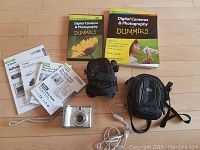 Photo of all items in the lot including camera, user guides, USB cable, camera cases, unopened SD card, and the photography book and DVD.