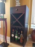 View of the entire bar cabinet showing the drawer, X-shaped wine rack with bottles, hanging rack, and bottom liquor storage.