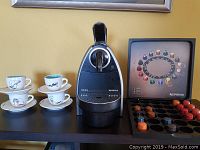 Black and silver Nespresso Essenza machine with shoe-themed espresso cups and decorative box with coffee pods