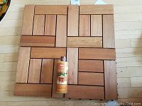 Topview of four wooden interlocking floor tiles arranged in a square with a bottle of outdoor furniture wax placed on top.