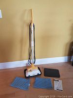 Machine assembled standing on hardwood floor against yellow wall with handle up, power cord coiled, and accessories laid out
