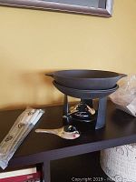 Cast iron fondue pot assembled on black metal stand with small burner underneath, six fondue forks in sealed packaging and a small stainless steel spoon on shelf beside set.