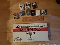 Eight decks of playing cards arranged alongside wooden cribbage board and unopened Classic Monopoly game on floor