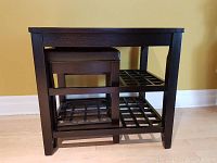 Side view of dark brown wood side table nesting cushioned leather stool under it, showing lattice shelves and furniture style.