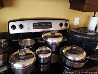 Full image showing multiple stainless steel pots with lids and one black speckled roasting pan on a stove.
