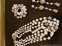 Photo showing 4-strand pearl and gold necklace, matching bracelet, and long dangle pierced earrings on dark background.