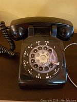 Front angle view of the black rotary phone showing the dial, handset, and coiled cord