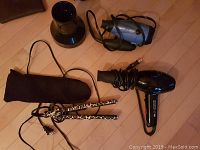 Full lot display showing black professional hair dryer with diffuser, blue Conair Ion Shine travel hair dryer, leopard print flat iron and case on a light wood floor.