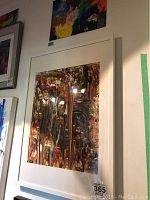 Framed abstract painting by Alex Hare with brown, black, red, yellow vertical dripping colors, white mat and frame, front view.