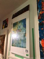 Framed abstract artwork by Alex Hare showing blue, green, yellow, and red colors with geometric shapes, mounted on a white wall.